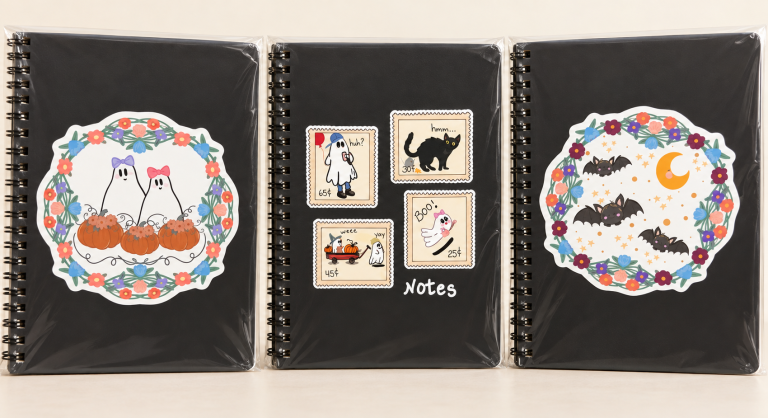 Three black spiral notebooks featuring floral ghosts, Halloween postage stamps, bats and a crescent moon.
